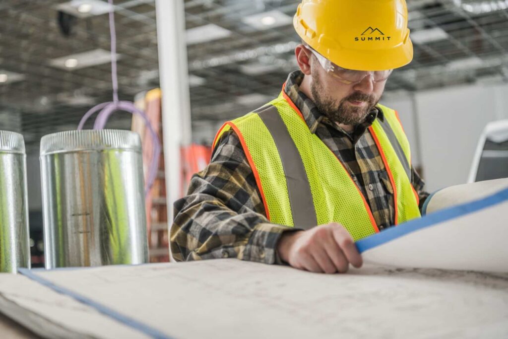 Construction worker in safety gear reviewing blueprints on a worksite, highlighting Summit Service Solutions' commitment to skilled labor staffing and career development.